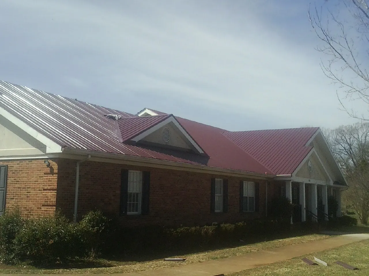Red metal roof with gabled entries on a long brick building, from a Hail Damage Roof Repair job in Daytona Beach