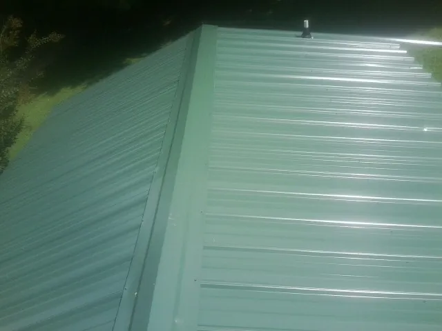 New green metal panels meeting at the ridge of a roof — Flat Roof Repair work by our crew in Daytona Beach