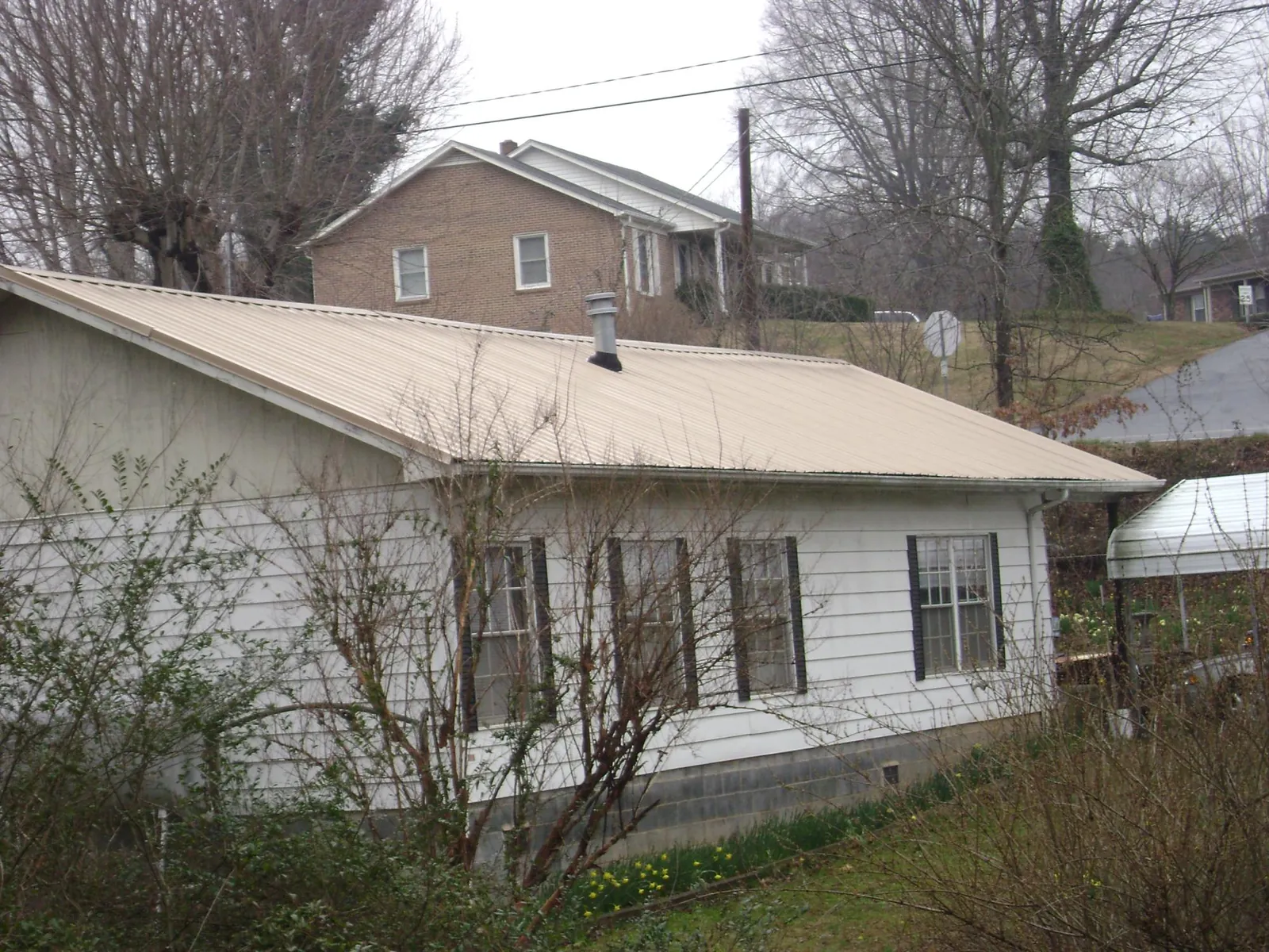Tan metal roof on a white sided house set into a hillside — Commercial Roofing by Roofing Brothers in Daytona Beach