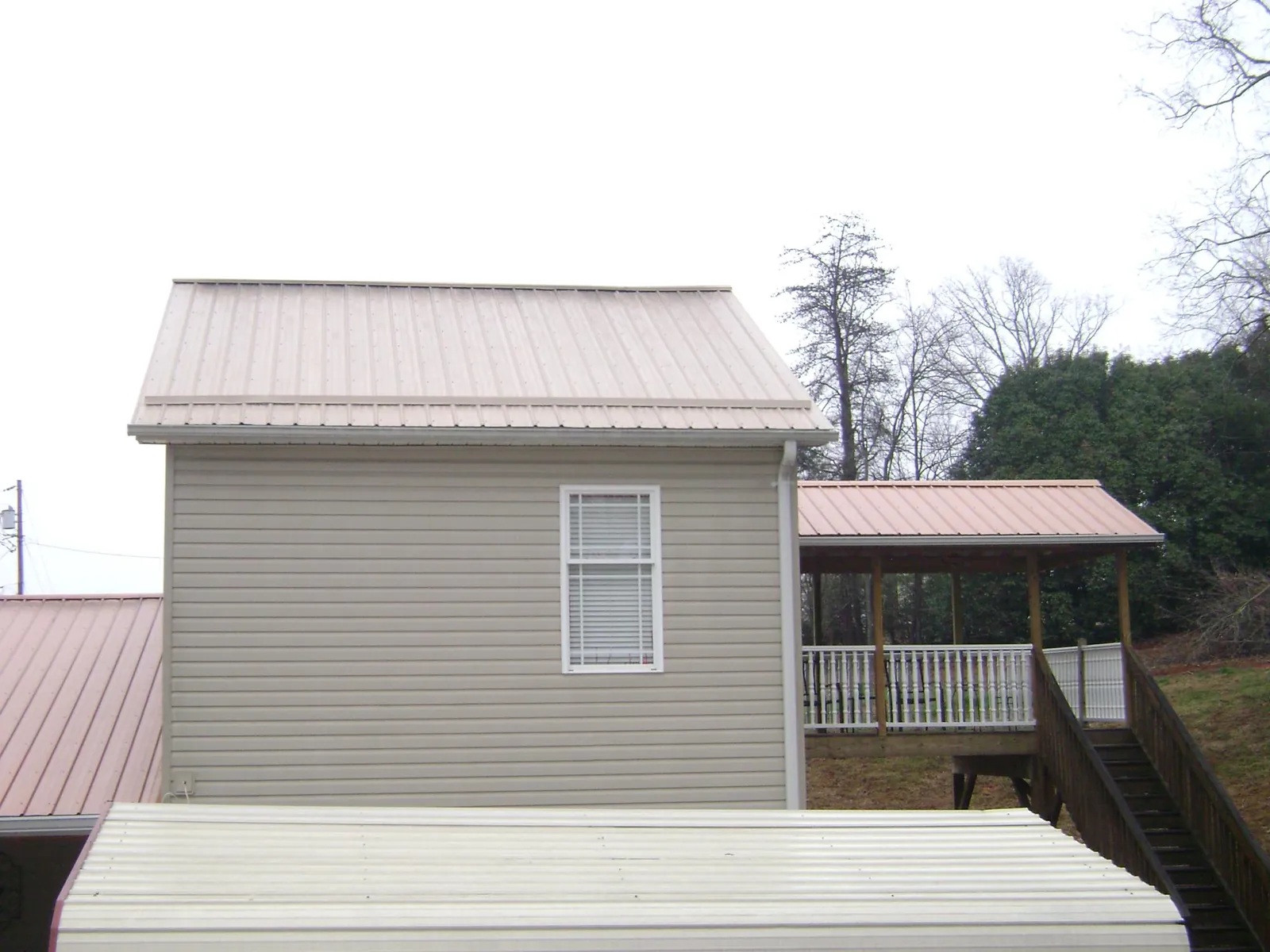 Tan metal roofs on a two story addition and attached porch, from a Roof Replacement job in Daytona Beach